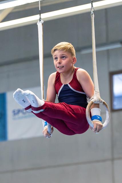 Young athlete performing on still rings, displaying focused concentration during routine at indoor sports facility