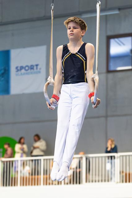 Young athlete suspended on still rings, displaying concentration and controlled form during routine at indoor sporting venue