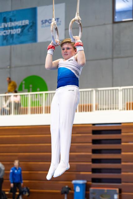 Young gymnast performing a hang position on still rings during competition, displaying focus and determination