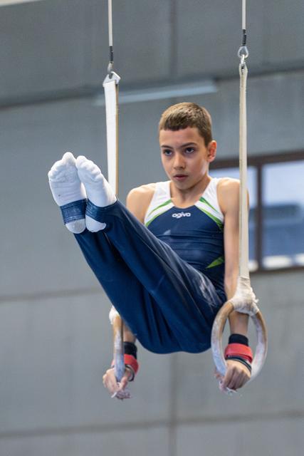Young gymnast performing a horizontal leg hold on rings, displaying focused concentration during training