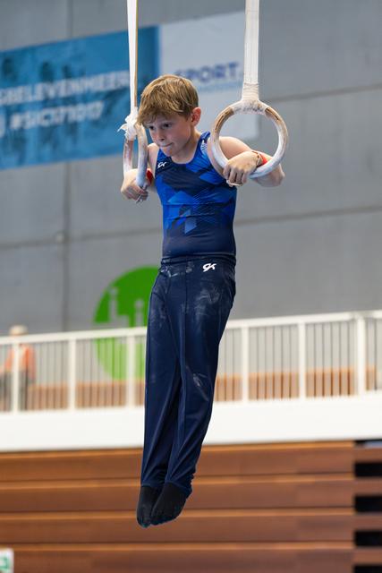 Young athlete practicing on still rings in blue uniform, concentrating during training session at indoor sports facility