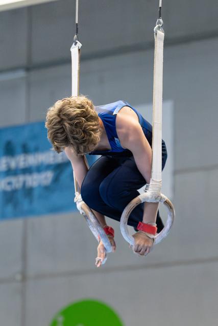 Young athlete performing an inverted hold on still rings during a routine, demonstrating strength and body control