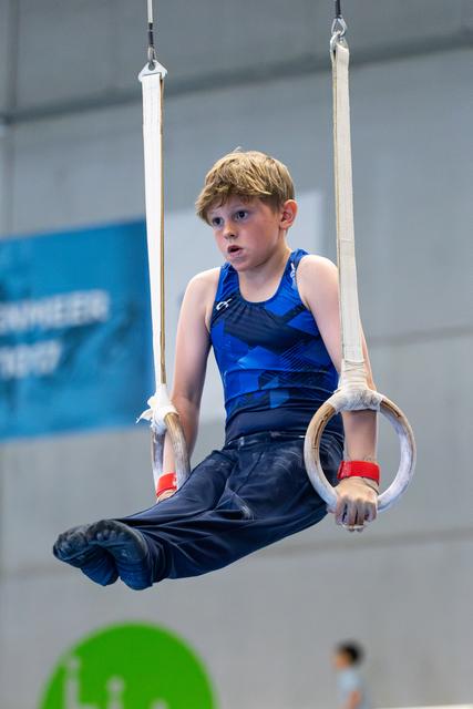 Young athlete suspended on rings during routine, displaying concentration with raised eyebrows in gymnasium setting