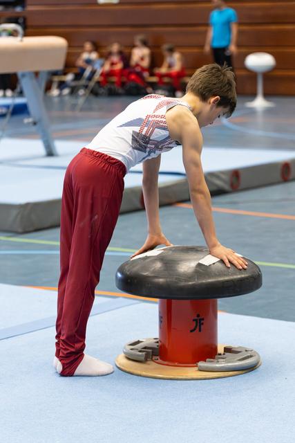 Young athlete practicing balance and strength on a mushroom trainer, leaning forward with focused concentration in a gym