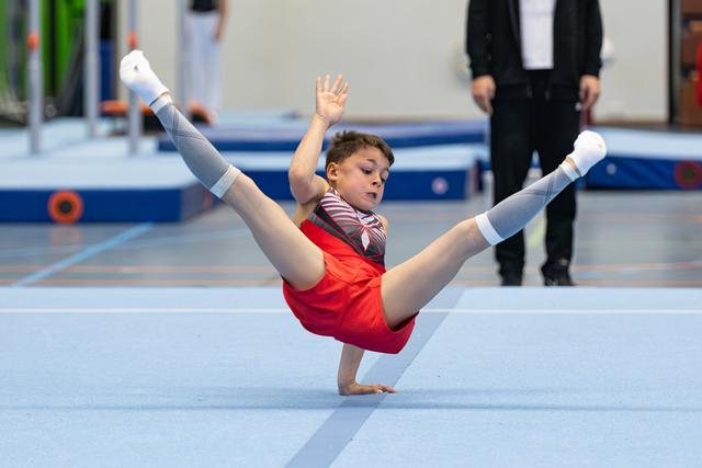 Young gymnast performing an impressive split leap during floor routine at indoor sports venue