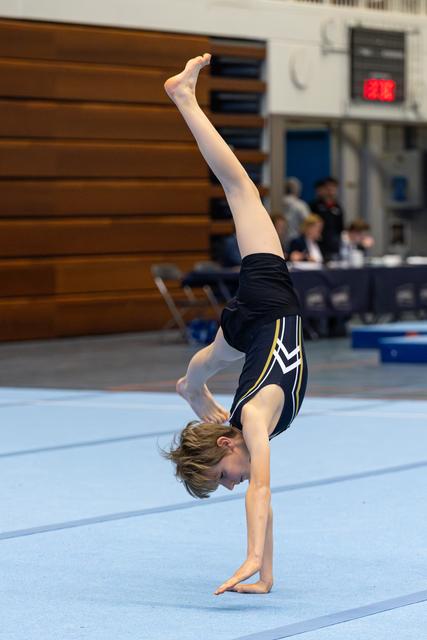 Young gymnast performs a graceful one-handed handstand during floor routine at indoor competition