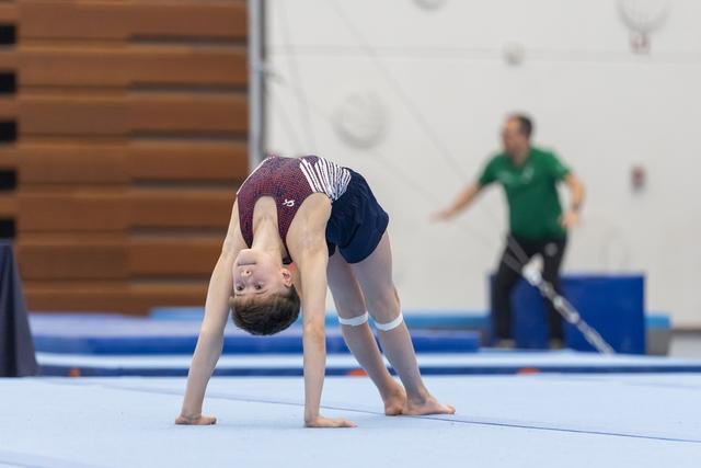 Young gymnast performs a back bend on blue floor mat, displaying impressive flexibility during training session