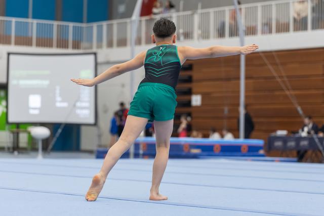 Young gymnast in green uniform performs an elegant pose during floor exercise routine at indoor gymnastics meet