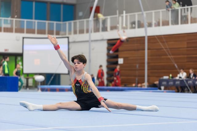 Young gymnast performs a split on the floor with one arm gracefully extended, displaying flexibility and poise in the arena