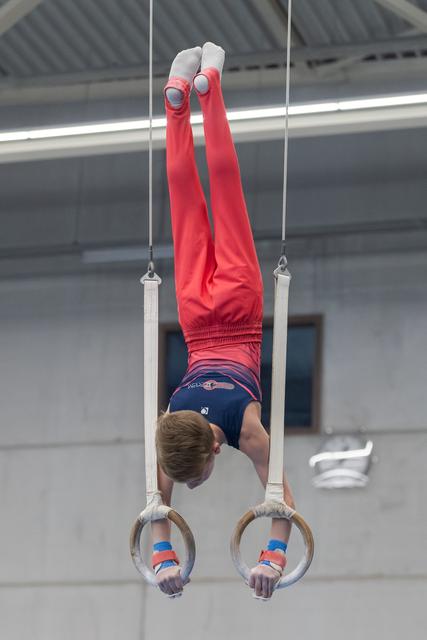 Male gymnast performing an inverted handstand position on still rings in an indoor training facility