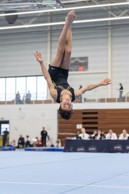 Gymnast executes an inverted aerial flip during floor routine, arms extended, at indoor gymnastics meet