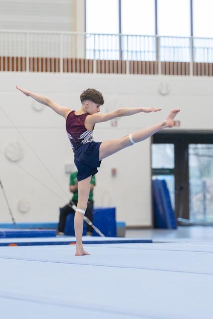 Young gymnast executes an elegant arabesque leap on floor exercise, arms extended gracefully in training facility