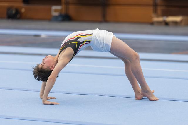 Young gymnast executes a backbend position on the floor mat, displaying flexibility and control during routine