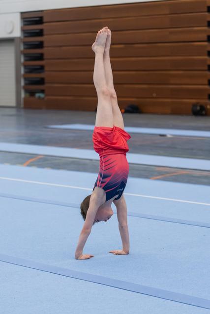 Gymnast executing a perfect handstand with legs extended vertically on blue mat in training facility