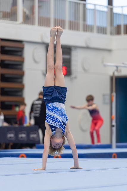 Young gymnast executes a steady handstand on the floor mat, legs extended vertically, during training session