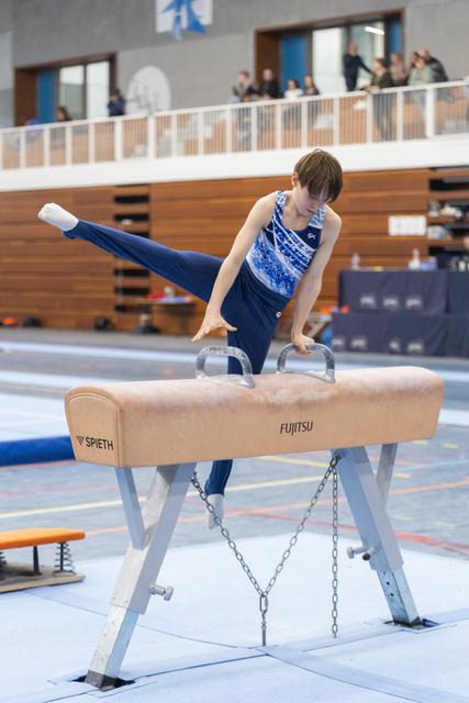 Young gymnast executes a scissor move on pommel horse, legs extended horizontally, displaying strength and control
