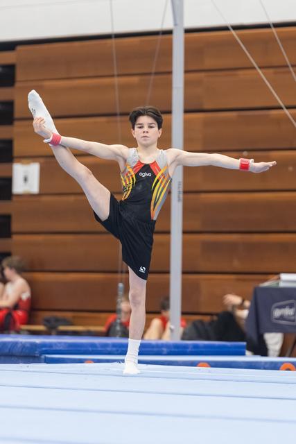 Male gymnast performs a front scale balance with extended leg during floor exercise routine in indoor gymnasium