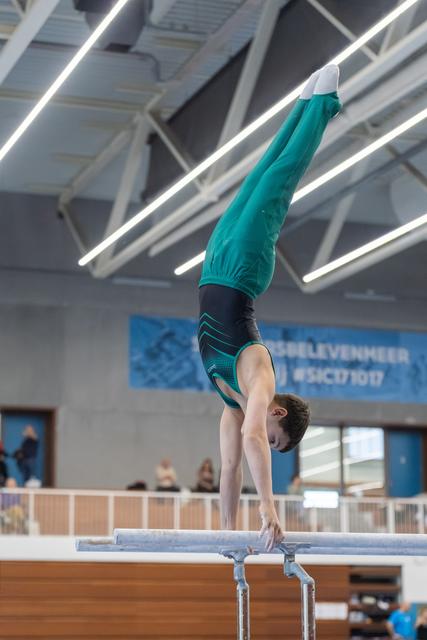 Male gymnast performing vertical handstand on parallel bars in indoor training facility with banner visible
