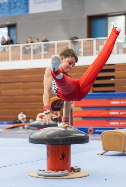 Male gymnast in red leotard executes a horizontal scissor move on pommel horse, demonstrating strength and control