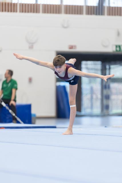 Young gymnast performs an arabesque balance with extended arms during floor routine at indoor training facility