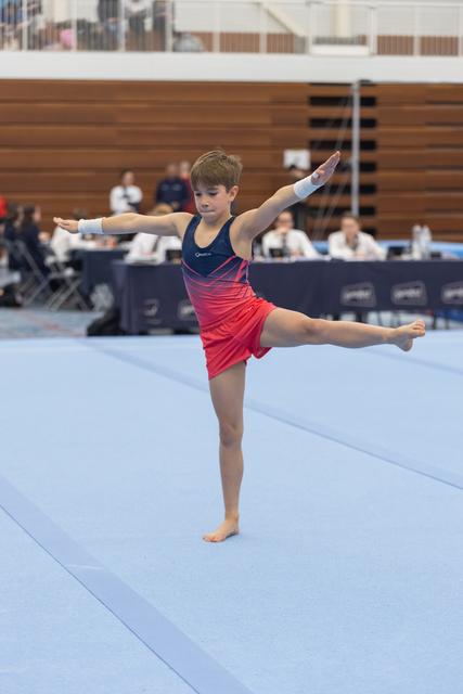 Young gymnast performs an arabesque balance on floor exercise, arms extended gracefully during her routine at indoor meet