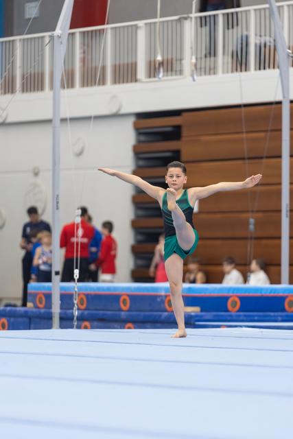 Young gymnast performs arabesque pose on floor exercise mat, arms extended, displaying balance and grace in teal leotard