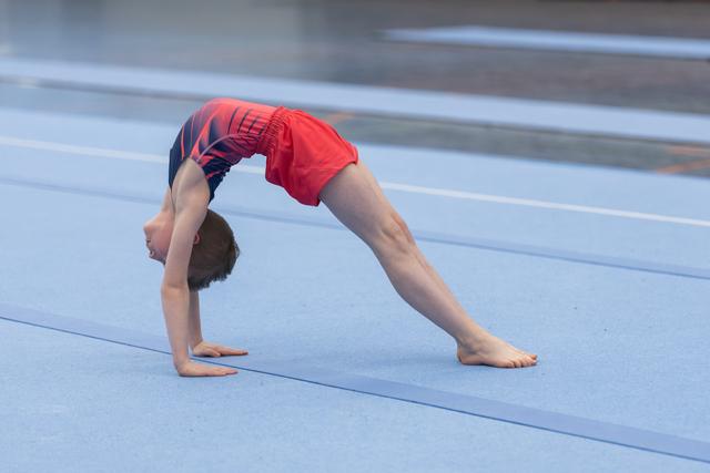 Young gymnast performing a deep backbend bridge on blue floor mat, demonstrating flexibility and strength