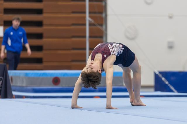 Young gymnast performs a backbend during floor routine, demonstrating flexibility and balance while coach observes in background
