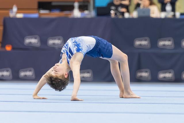 Young gymnast performs bridge backbend on floor mat during routine, displaying flexibility and strength at indoor event