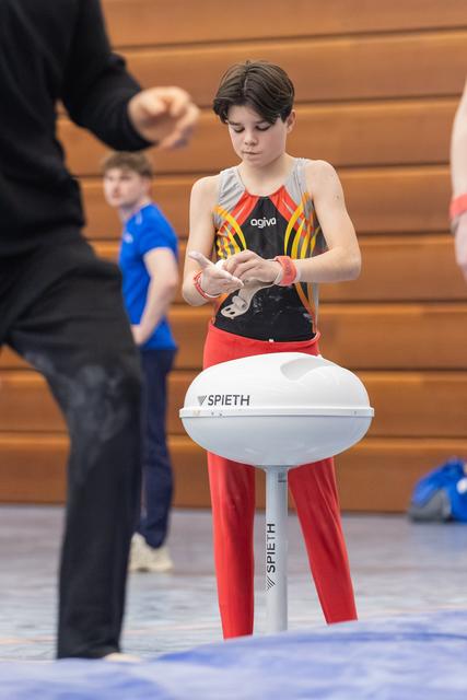 Young gymnast in colorful leotard carefully applies chalk to hands while standing at vaulting table, focused and preparing