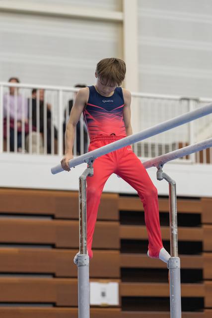 Young gymnast in red pants and gradient leotard focuses intently while performing on parallel bars in indoor training facility