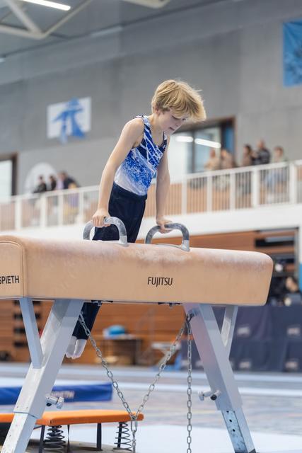 Young gymnast with blonde hair focuses intently while gripping pommel horse handles during training session
