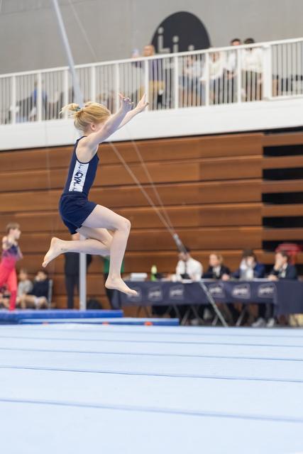 Young gymnast in navy leotard performs an elegant leap during floor exercise routine at indoor gymnastics meet