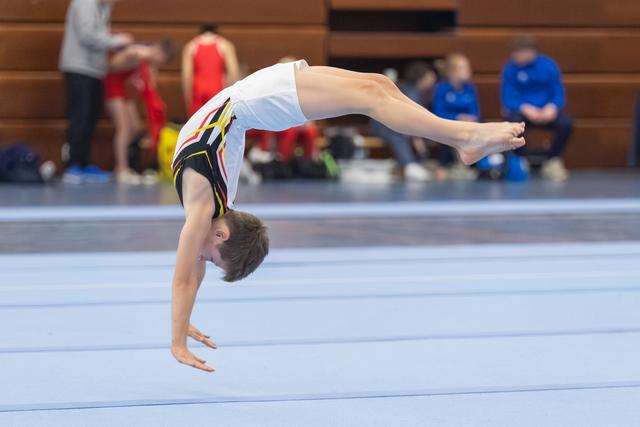Young gymnast performs a flexible backbend on floor mat during routine, demonstrating strength and control