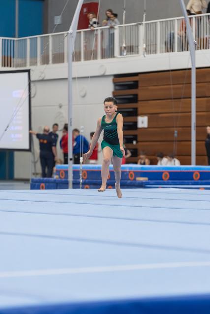 Young gymnast in teal leotard performs floor exercise routine with focused expression on competition mat
