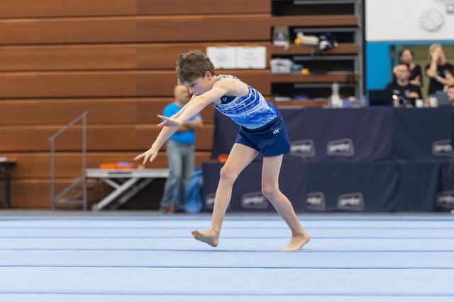 Young gymnast in blue sequined leotard performing expressive floor routine with extended arms and focused posture