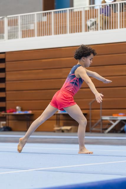 Young gymnast performs graceful leap position during floor routine, arms extended with focused expression in training gym