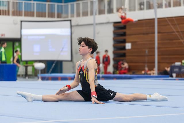 Young gymnast performs a splits position on floor exercise mat during routine at indoor gymnastics meet