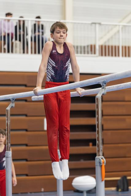 Young male gymnast performing on parallel bars wearing navy sequined leotard and red pants in indoor gym facility