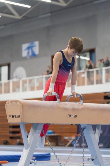 Young gymnast concentrates on pommel horse, gripping handles with determination during training session in gym facility