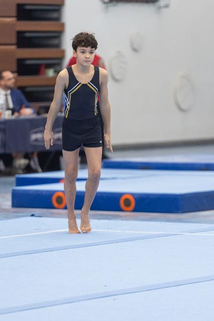 Young gymnast in navy leotard walks barefoot on floor exercise mat, displaying focused concentration before routine