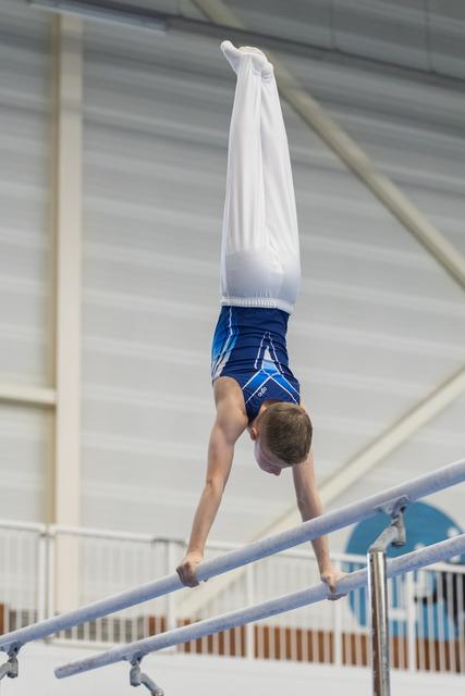 Young gymnast performs a handstand on parallel bars during training, displaying strength and balance in the gym
