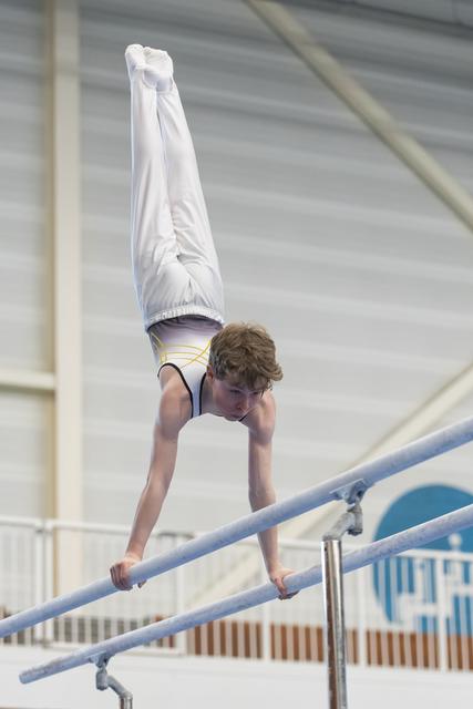 Young gymnast performing a handstand on parallel bars, legs extended straight up, in an indoor training facility
