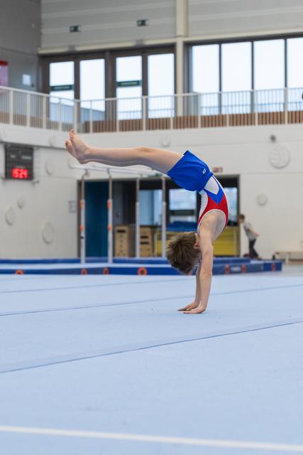 Young gymnast holds a precise handstand position on the blue floor mat, demonstrating strength and balance during training.