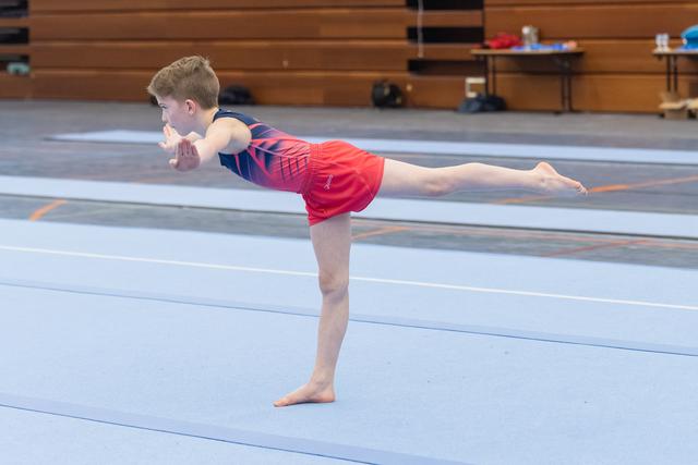 Young gymnast demonstrates horizontal balance pose on floor mat, arms and back leg extended in perfect alignment