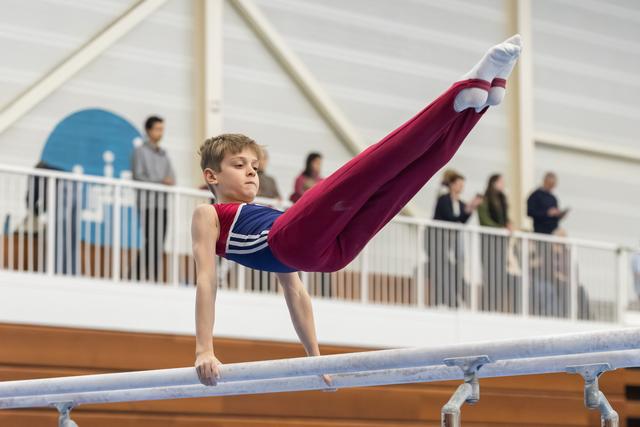 Young gymnast demonstrates impressive strength on parallel bars with extended legs during training session