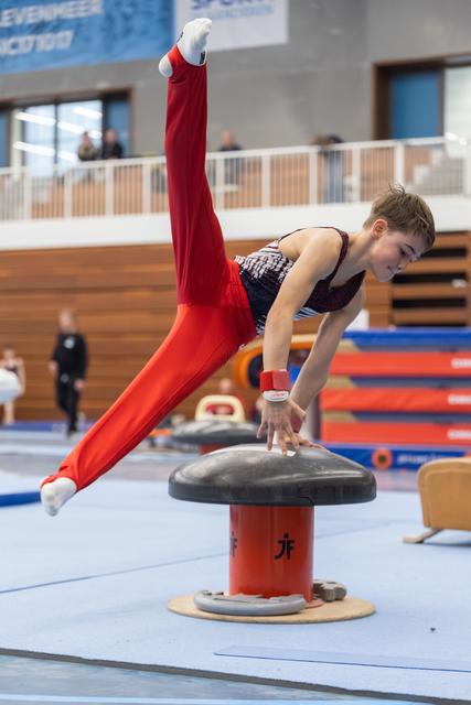 Young gymnast performing a horizontal hold on pommel mushroom, demonstrating strength and control in red tracksuit