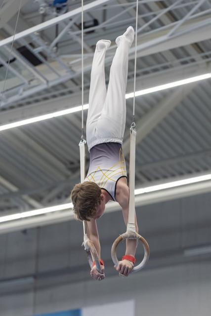 Young male gymnast performing an inverted hold on still rings in an indoor training facility, demonstrating strength and control