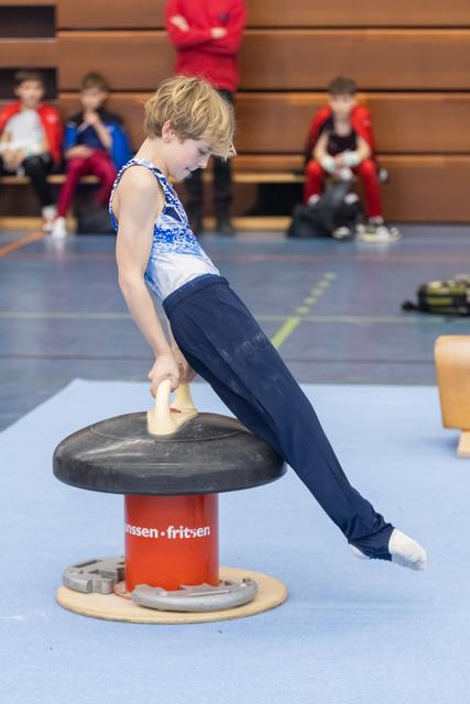 Young gymnast performs a support hold on a mushroom circle apparatus, extending his body horizontally in a training gym
