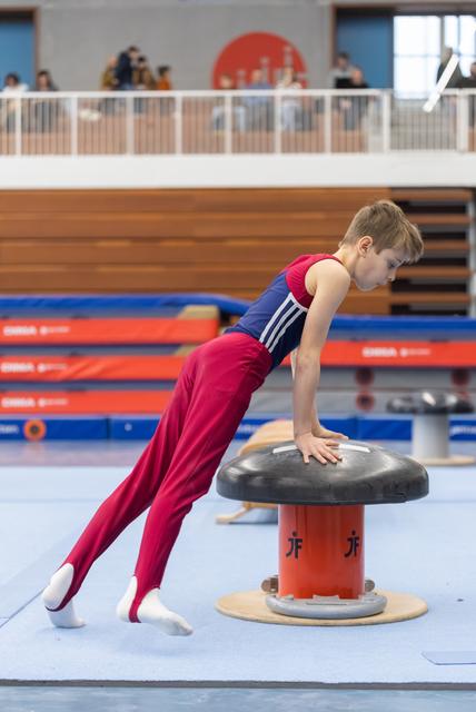 Young gymnast in burgundy and navy uniform performing a plank position on mushroom apparatus during training